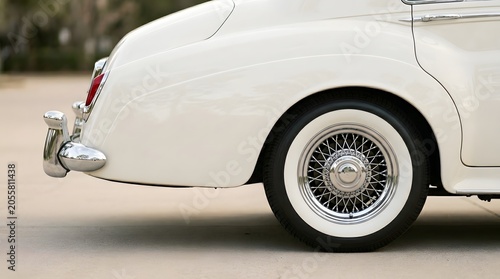 Rear fender and wire spoke wheel with whitewall tire on white vintage luxury car