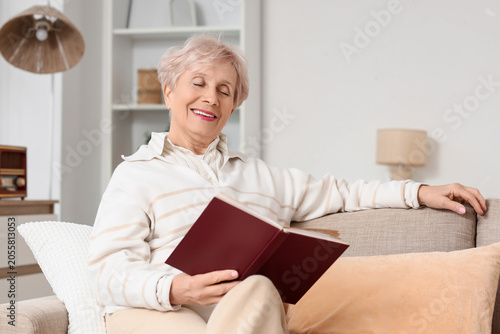 Beautiful senior woman reading book on sofa at home