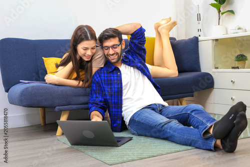 Business couple working, communicating while sitting at the home office desk together. Cheerful couple, calm asian woman and caucasian man working at home with laptop together.