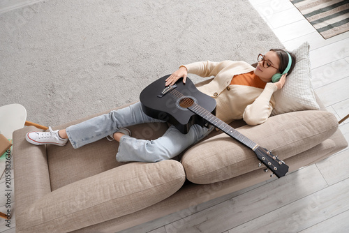 Portrait of young girl with guitar listening to music while lying on sofa at ...