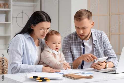 Young couple with calculator and their baby planning budget at home