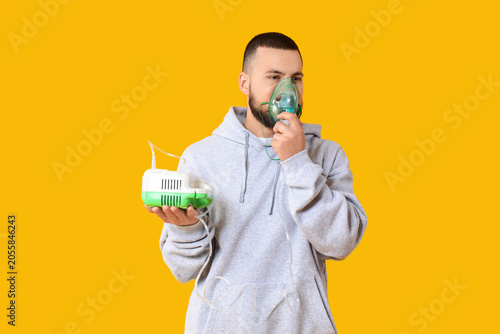 Young man using nebulizer on yellow background