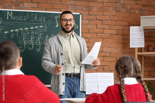 Принти на полотні Smiling male music teacher with baton and sheet music instructing young students