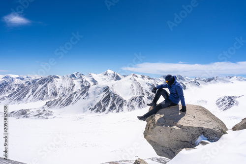 Mountain Climber Sitting on Summit Rock Overlooking Vast Glacial Panorama of Tsambagarav Range, Mongolian Altai
