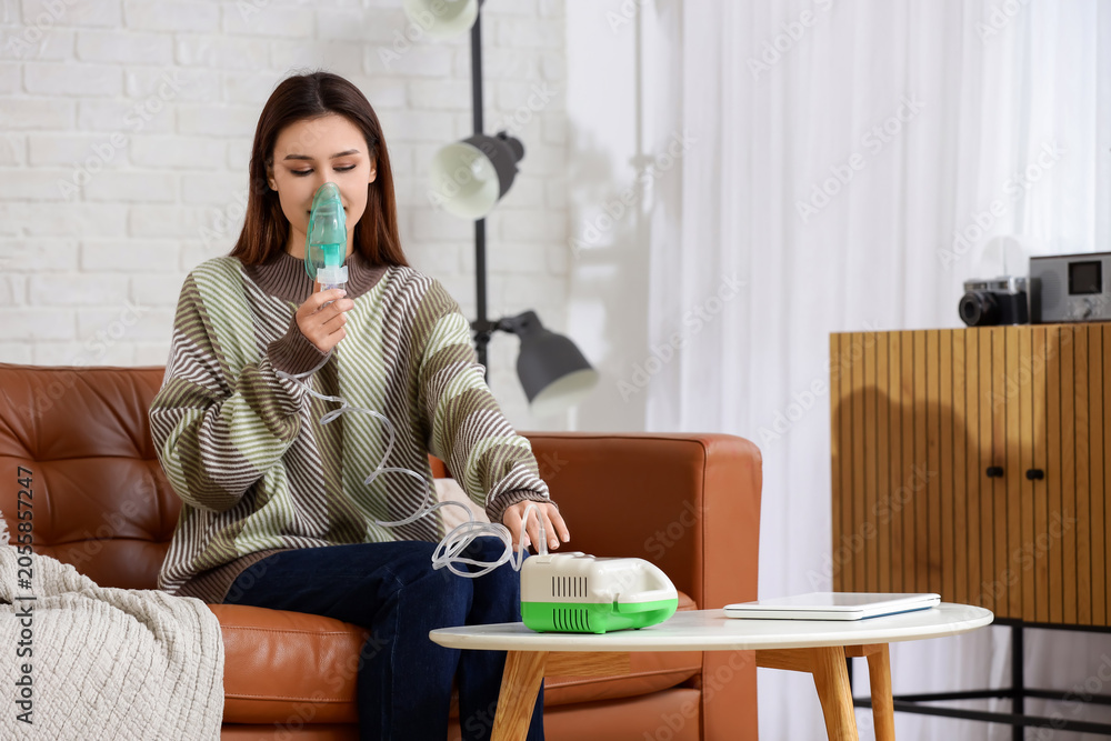 Obraz premium Young woman using nebulizer on sofa at home