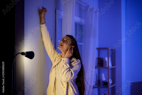 Young woman knocking on wall because of noisy neighbours at home late in evening