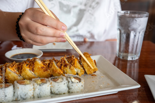Person using chopsticks to eat crispy tempura sushi roll