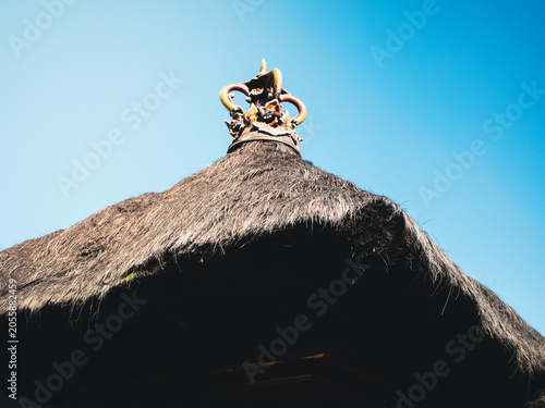 Balinese temple roof with layered thatch and ornate sacred ornament at the apex, set against a vivid blue sky — traditional Hindu architecture reflecting local craftsmanship and spirituality