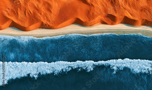 Aerial view of rolling desert dunes meeting a sandy beach and ocean waves