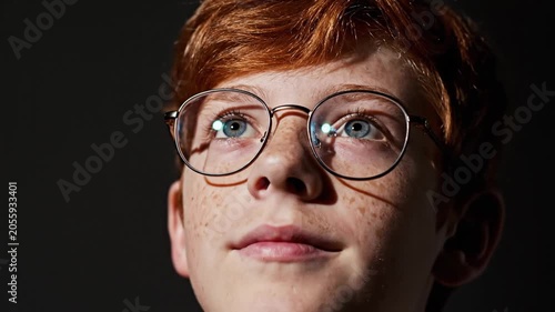 Redheaded boy with freckles and round glasses rolling his eyes back in a dark studio
