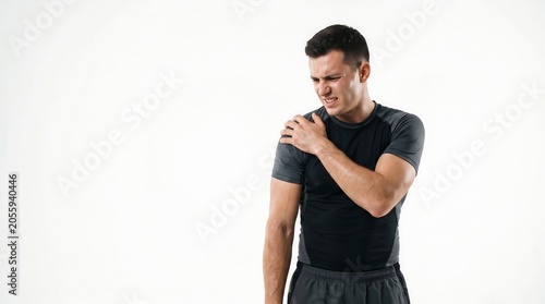 Young athletic man in sportswear suffering from shoulder pain and holding his injured joint with a grimace against a white background