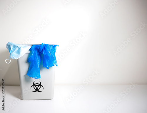 View of pail blue nitrile gloves were thrown into a biohazard bin on grey room background. Medical for disposable glove.