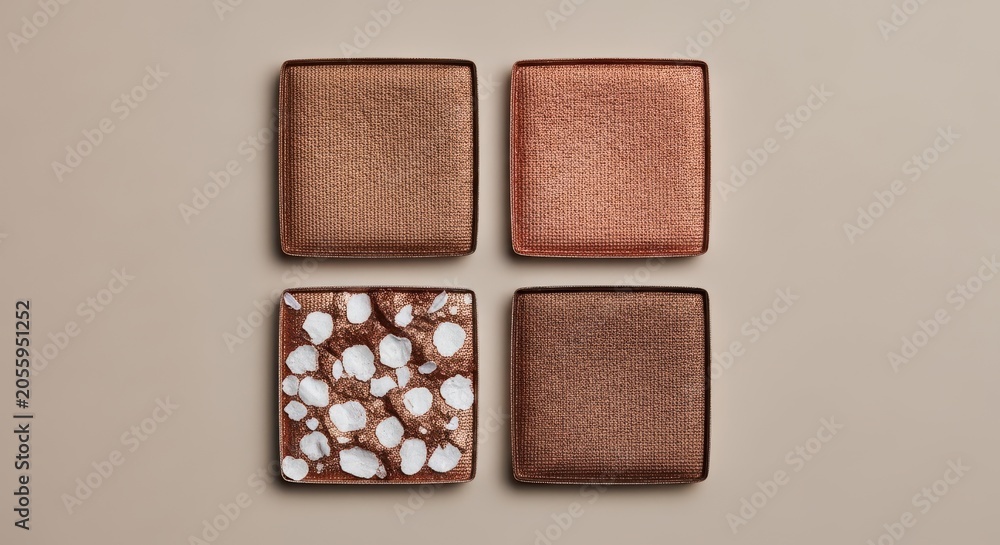 Fototapeta premium Four square eyeshadow pans in various bronze and copper metallic shades on a neutral background