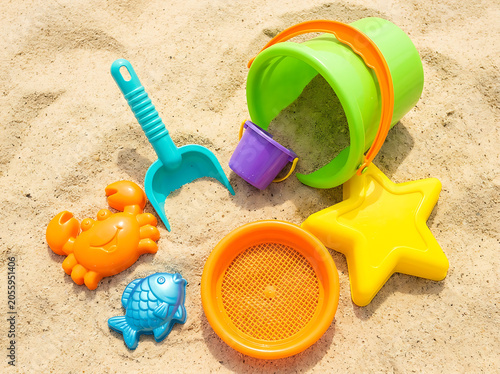 High angle view of vibrant plastic beach toys including buckets, sifter, shovel, crab, fish, and star molds scattered on fine sand.
