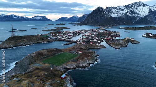 Scenic Drone Flyover of Henningsvaer Soccer Field Encircled by Arctic Ocean and Snowy Mountains, Lofoten Norway at blue hour, horizontal drone shot