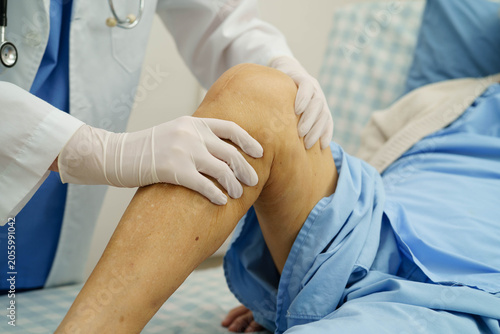 Doctor checking Asian elderly woman patient with scar knee replacement surgery in hospital.