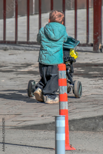 A boy plays with a baby carriage on the sidewalk on a spring day