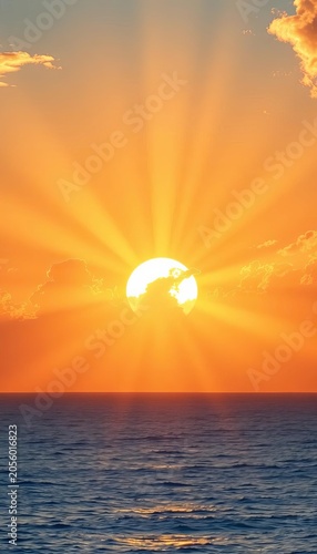 Vibrant sunrise over calm ocean, sunbeams pierce through wispy clouds, blue sky, dawn