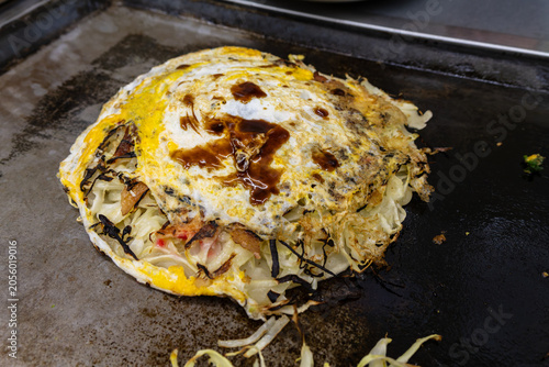 Foto japanese okonomiyaki with fried egg and sauce on teppanyaki grill