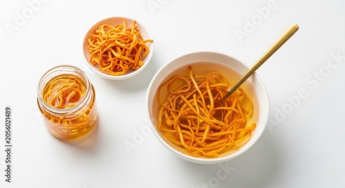 Cordyceps militaris mushrooms in a bowl and a glass jar with a golden spoon on a white background