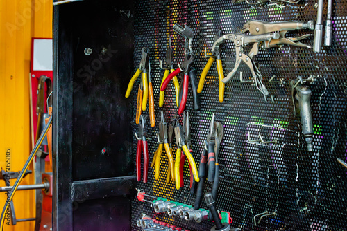 Professional pegboard tool wall in a mechanic's workshop, various pliers, locking pliers, assorted hand tools. Authentic  precision automotive repair, industrial maintenance, skilled mechanical work.