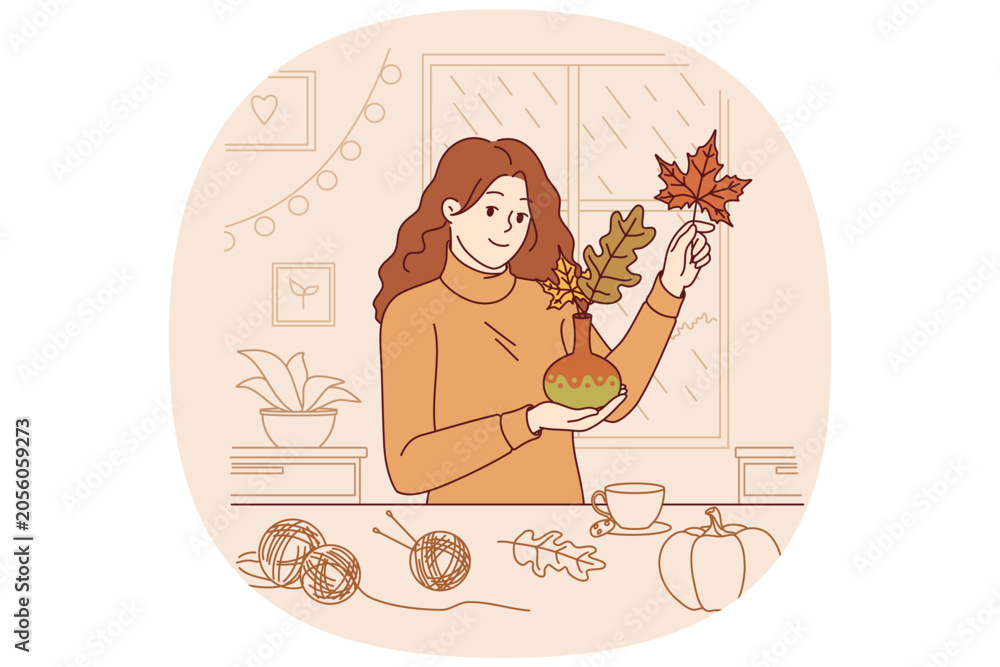 Fototapeta premium Woman collects bouquet of autumn leaves and places them in vase to decorate home on thanksgiving eve. Girl rejoices at arrival of autumn and makes decorations for apartment, creating cozy atmosphere