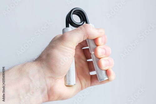 A man's hand squeezes and unclenched an expander to strengthen his grip on a gray background, close-up.