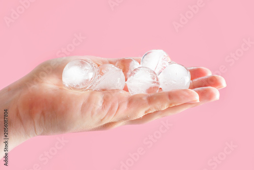 A woman's hand holding ice balls on a pink background close-up.