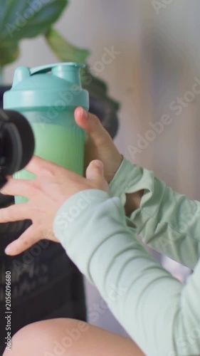 Vertical video: Reaching her lifting teal shaker to camera on mic cue, lounge, mint top, copy space