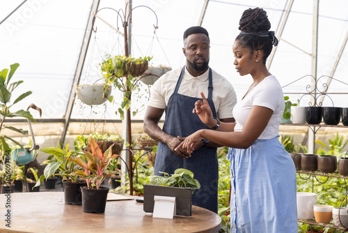 African American staff in blue apron and client talking about plants at nursery pointing at tablet