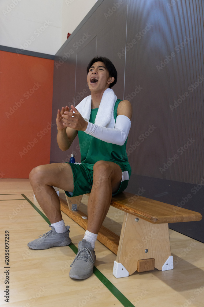 Naklejka premium Basketball player sitting on bench, clapping and shouting at court, towel and blue bottle nearby