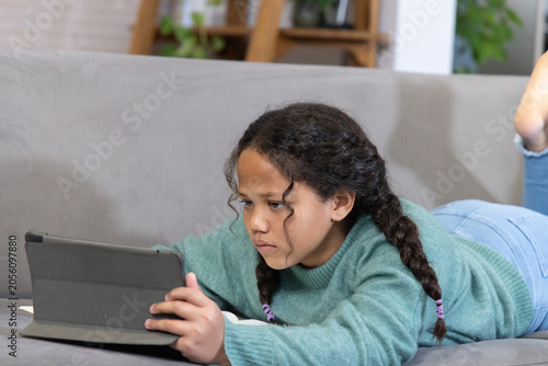Принти на полотні School-aged girl lying on gray sofa holding tablet in folio case, wearing teal s