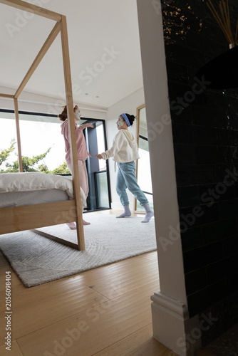 Two teenage females standing in bedroom by bed and glass door, wearing sheet masks and headbands