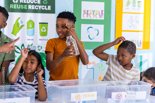 Diverse school-age children sorting recycling at classroom table, labeled PLASTIC bins and bottle