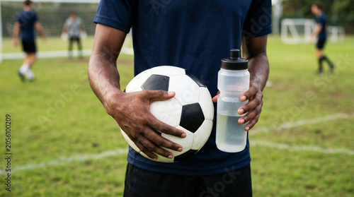 Extreme close-up of a soccer player holding a classic football and a bottle of drinking water on a green grass field, minimalist sports hydration and fitness concept