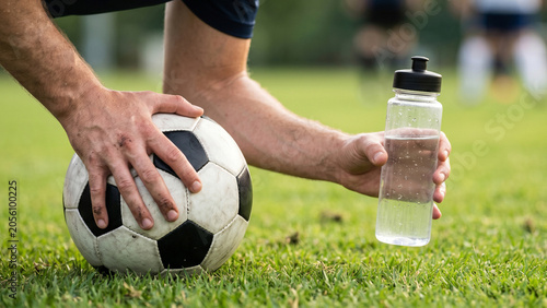 Extreme close-up of a soccer player holding a classic football and a bottle of drinking water on a green grass field, minimalist sports hydration and fitness concept
