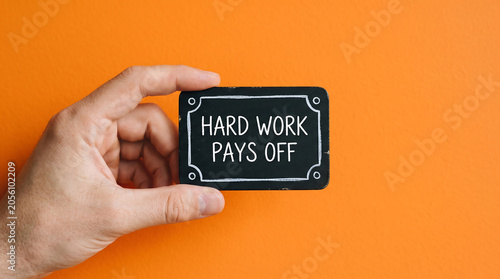 Inspirational motivational quote, hard work pays off, hand holding sign, black and white text on orange background, business motivation concept