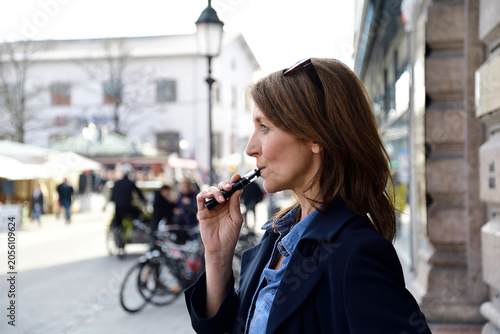 Mature woman smoking electronic cigarette in the city