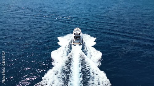 Aerial tracking shot of motorboat speeding across open deep blue ocean leaving twin white wake trails under bright midday sunlight