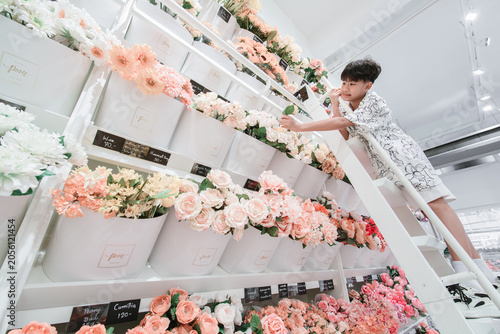 Young boy reaching for peach color flower on top shelf in flower shop