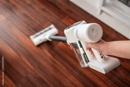 Tableau sur toile First-person perspective (POV) of a woman using a powerful white cordless vacuum cleaner on a dark hardwood floor, ergonomic design for effortless home hygiene and spotless surface