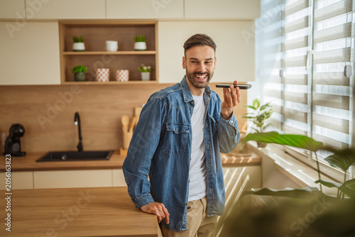 Bild auf Leinwand Man smiling using smart phone speakerphone sending voice message