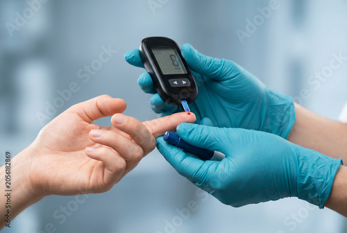 Medical professional in blue gloves testing blood glucose on a patient's finger with a glucometer.