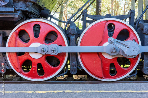Obraz na plátne A close-up view highlights the vibrant red driving wheels and mechanical linkage of a vintage steam locomotive resting on railway tracks at an outdoor museum setting