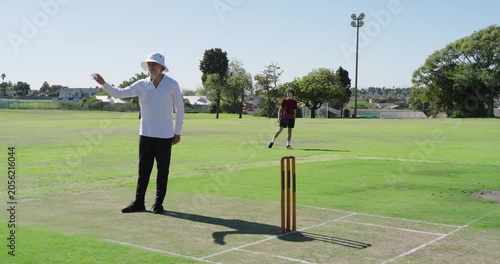 Umpire signaling bowler jogging to crease to begin over, batsman taking guard on pitch