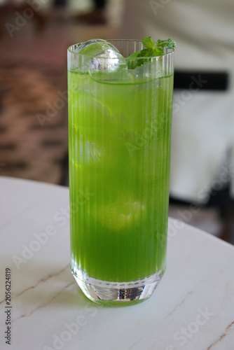 Refreshing bright green beverage served in a tall ribbed glass with ice cubes and fresh mint garnish.