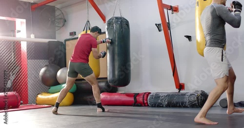 Diverse sparring partners wrapping hands and practicing heavy bag drills in gym for speed