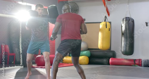 Following coach nodding, diverse coach and trainee practicing punching and kicking on pads at gym