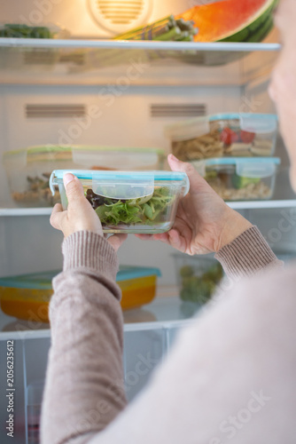 Woman Storing Healthy Meal Prep Containers in Refrigerator at Home. Close up
