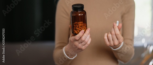 A close-up of a woman's hand holding a bottle of vitamin capsules and showing one tablet. Nutrient replenishment, healthy lifestyle